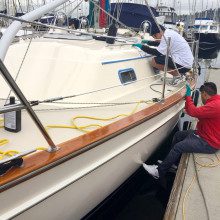 Two men working on a sailboat in a marina.